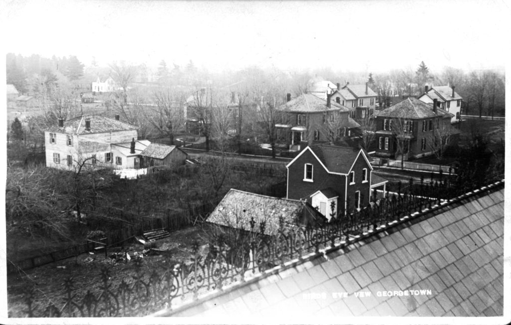 An old black and white photograph shows an aerial view of a neighbourhood with Victorian houses on large lots. 