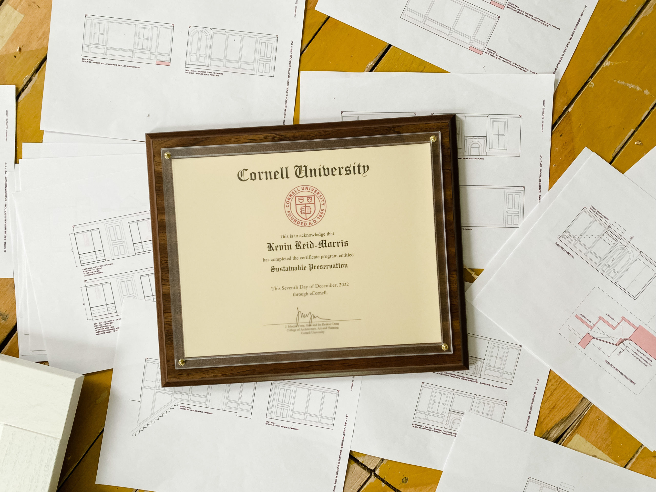 A graduation certificate that reads "Sustainable Preservation" from Cornell University sits amidst a set of building plans.