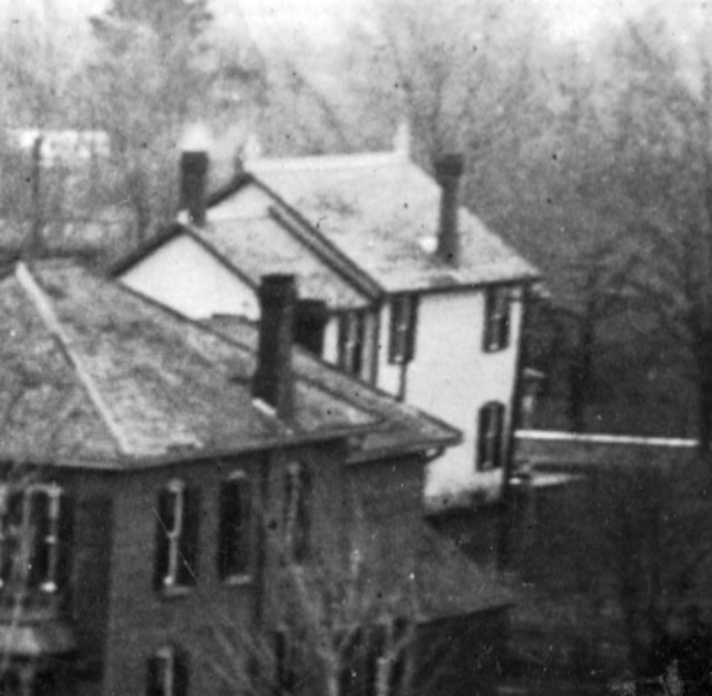 An old photo shows the back and side of a white Victorian house in the distance. 
